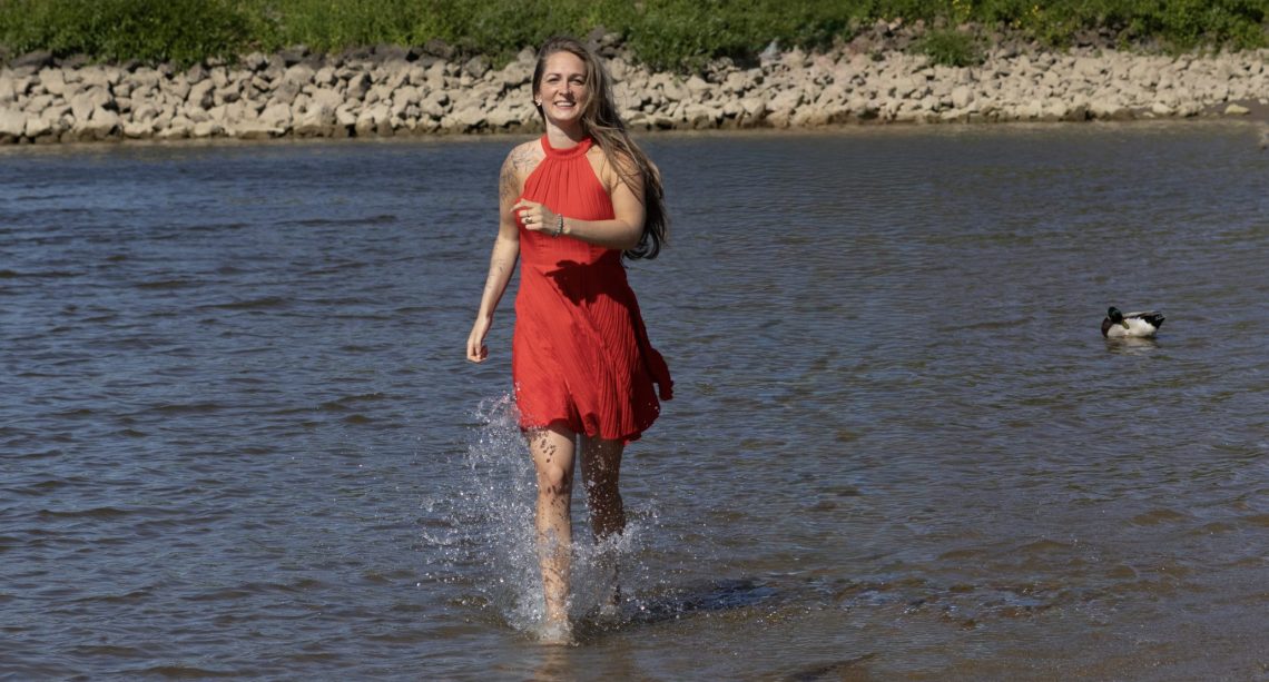 Vrouw in rode jurk lopend door water in de natuur, symbool voor persoonlijke groei en zelfherstel